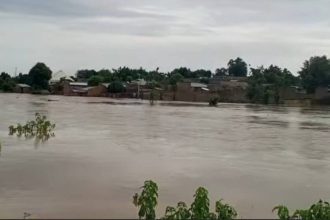 Flooded street in Nigeria with residents navigating water during heavy rainfall.